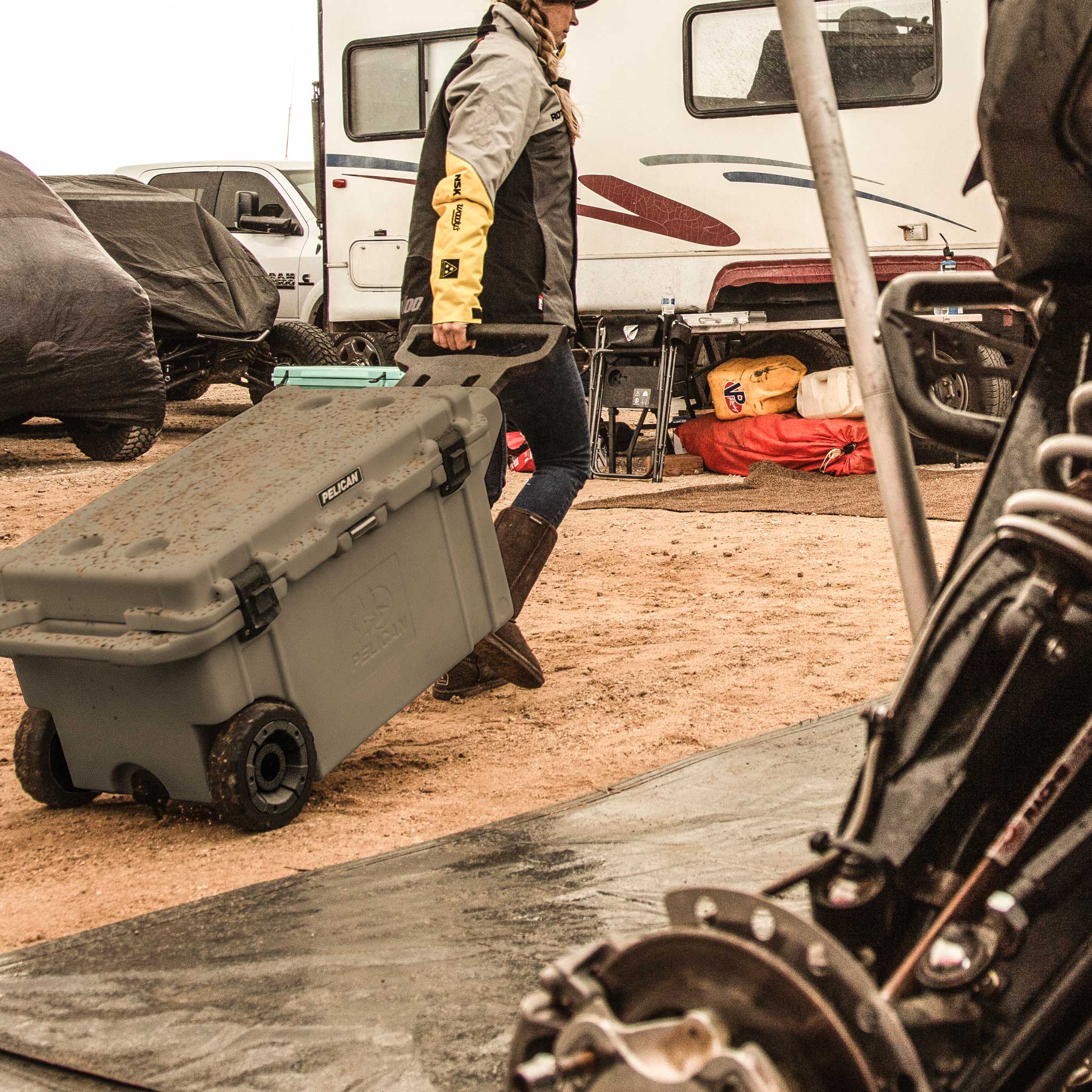 Charcoal 80QT Elite Wheeled Cooler being rolled across the dirt by it's handle