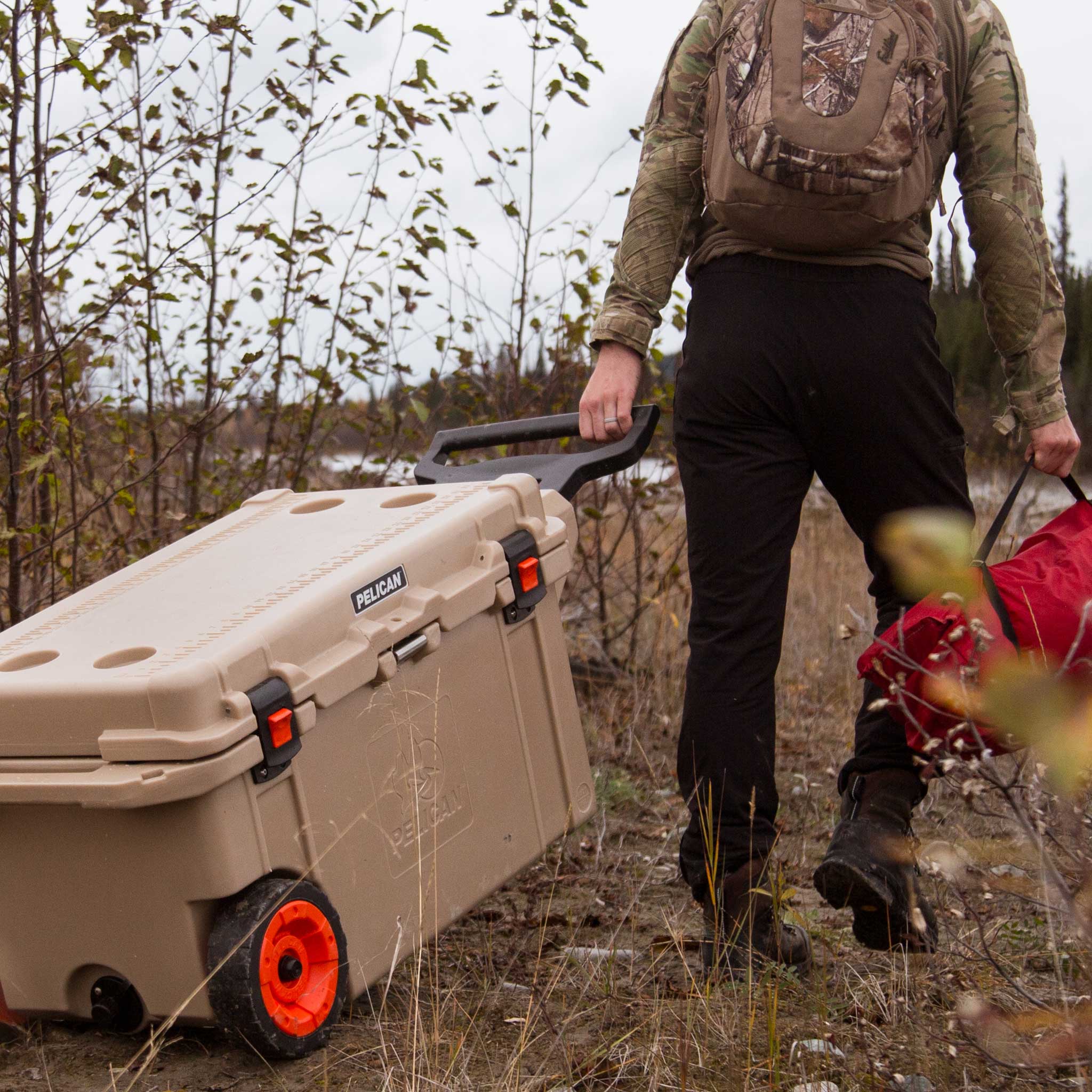 Desert Tan 80QT Elite Wheeled Cooler being rolled across the dirt by it's handle