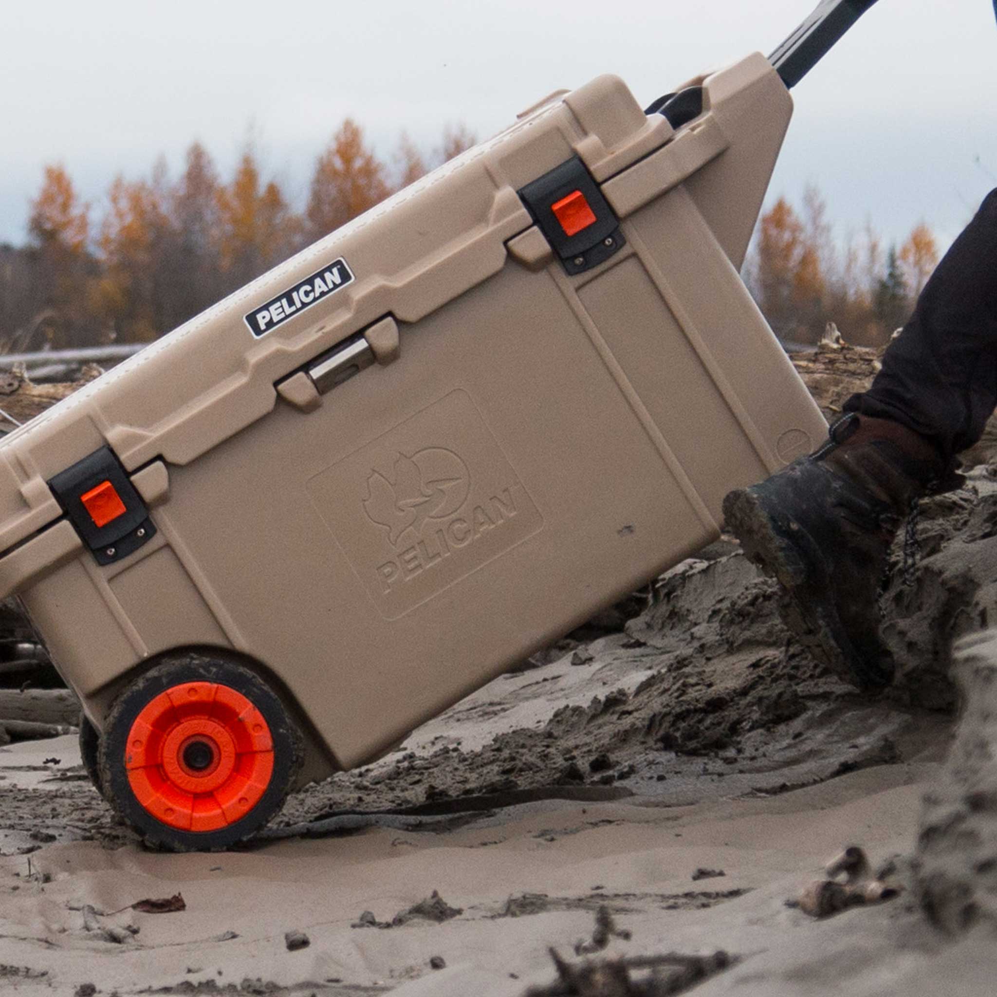 Desert Tan 80QT Elite Wheeled Cooler being rolled across the dirt by it's handle