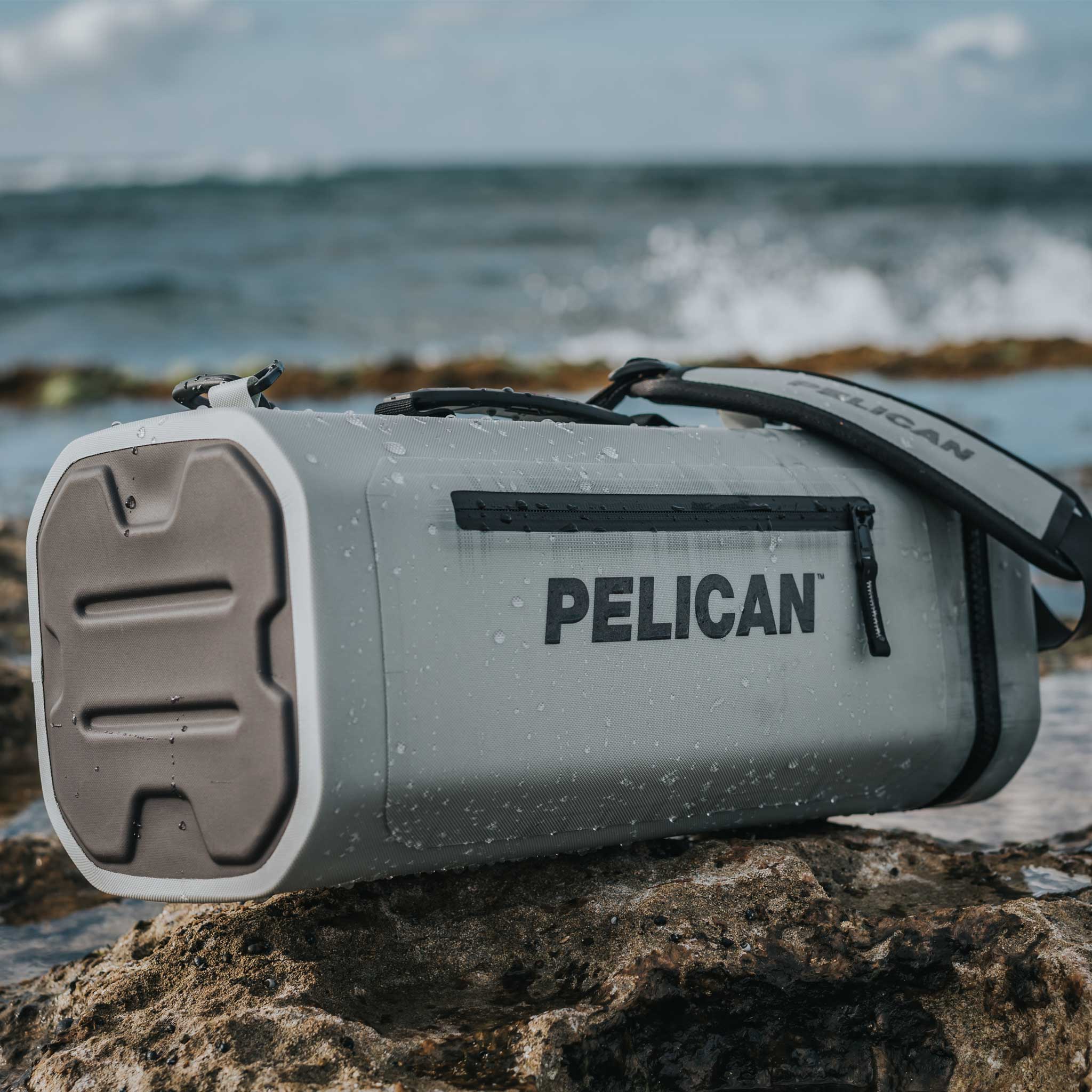 Light Grey Pelican™ Dayventure Sling Soft Cooler on the beach splashed with water